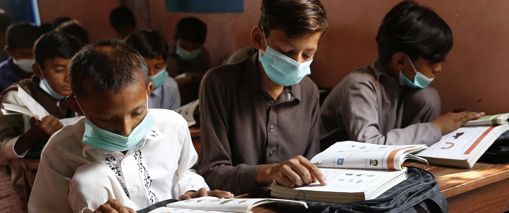 Three boys sat at a bench table reading from their school books