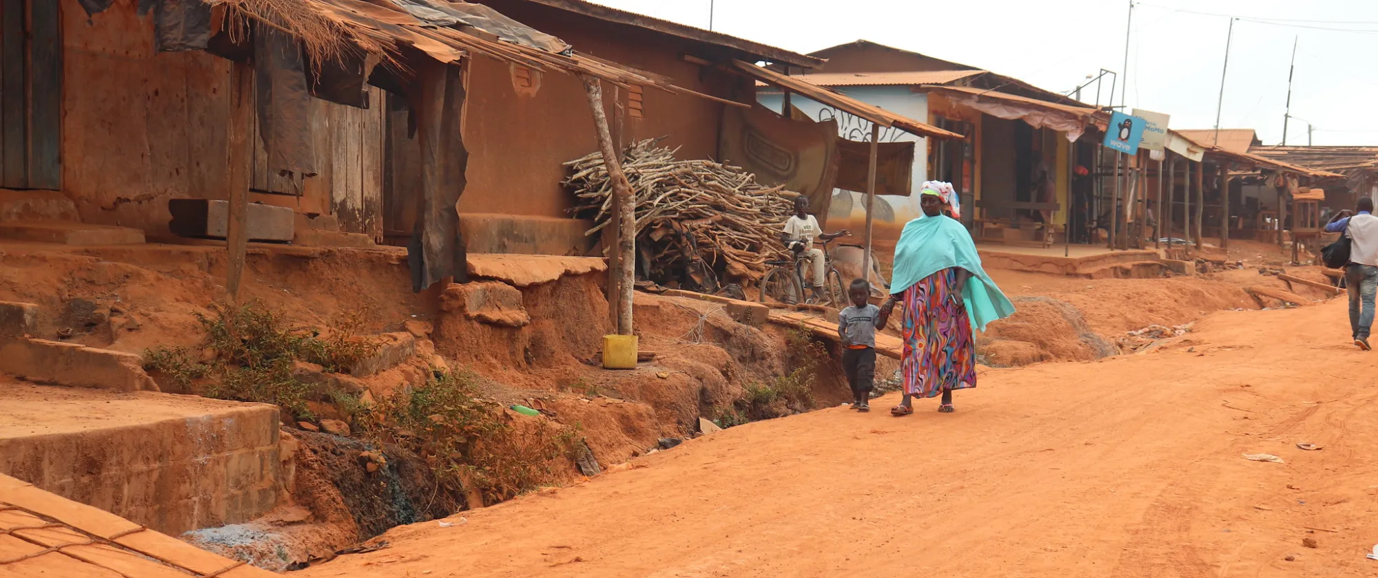 A women walks in an earth path of a community with a kid in her hand