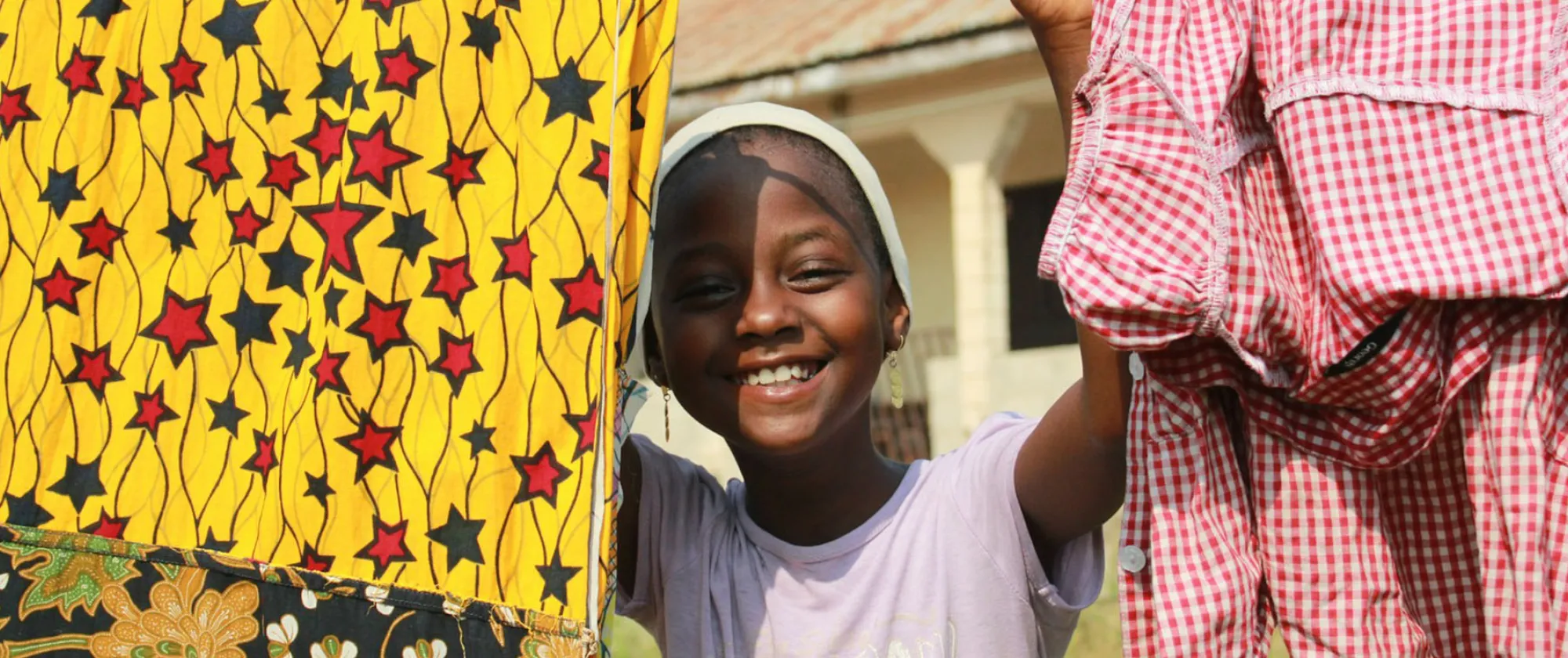 Smiling child in Abuja looks out from behind hanging laundry