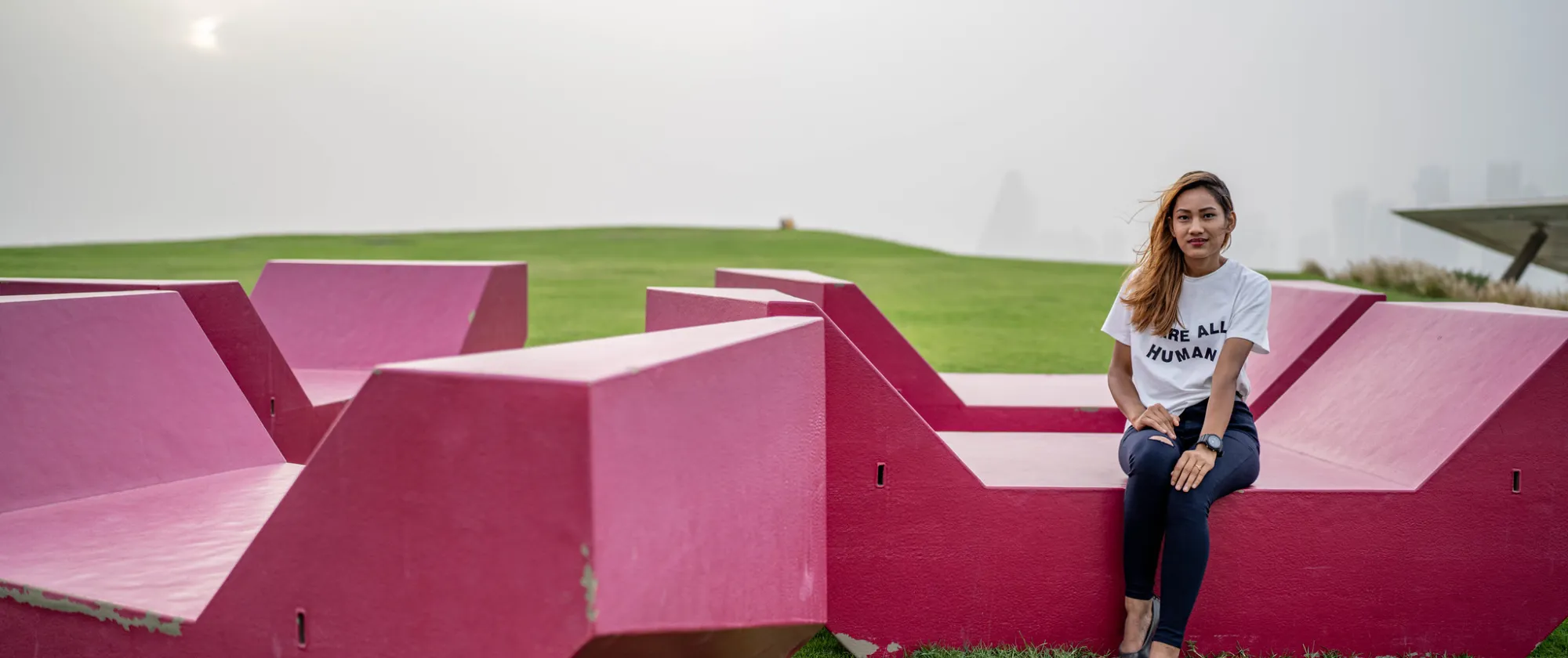 young lady wearing a tshirt We are all humans sitting on pink concret blocks in Qatar