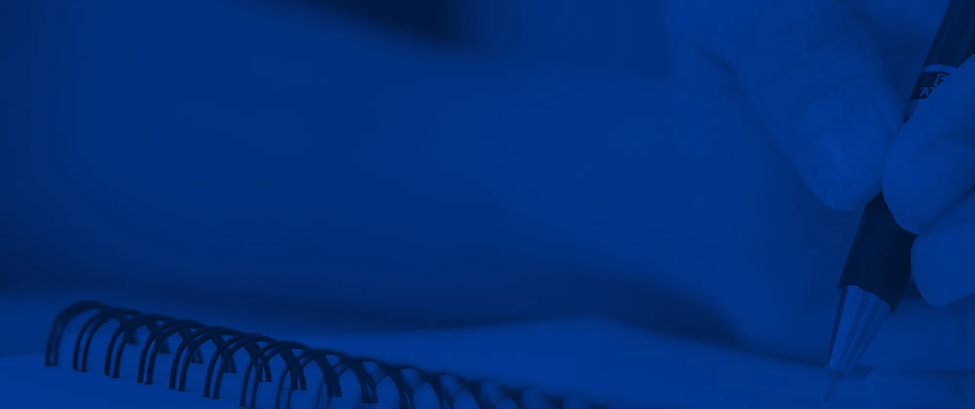 Una mano en primer plano escribiendo sobre un cuaderno, la imagen tiene un tono azul característico del proyecto SENATEC