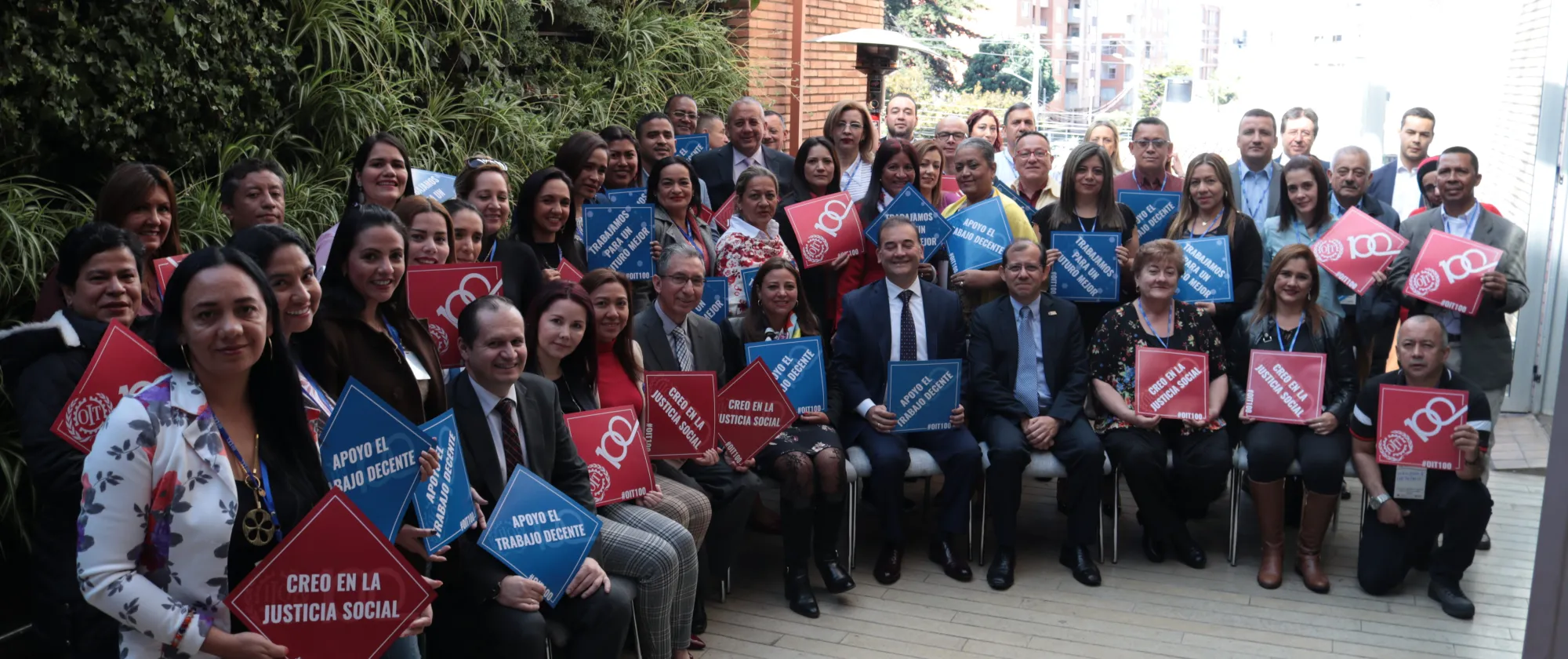 foto grupal de inspectores del trabajo de Colombia sosteniendo letreros alusivos a la conmemoraicón de los 100 años de la OIT como "apoyo el trabajo decente" y "creo en la justicia social"