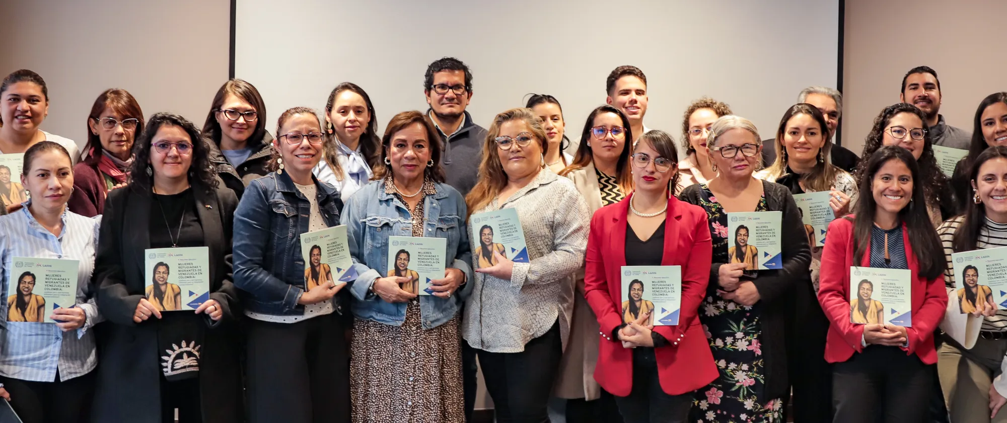 Fotografía de todas y todos los participantes del evento en plenaria sosteniendo en sus manos el informe