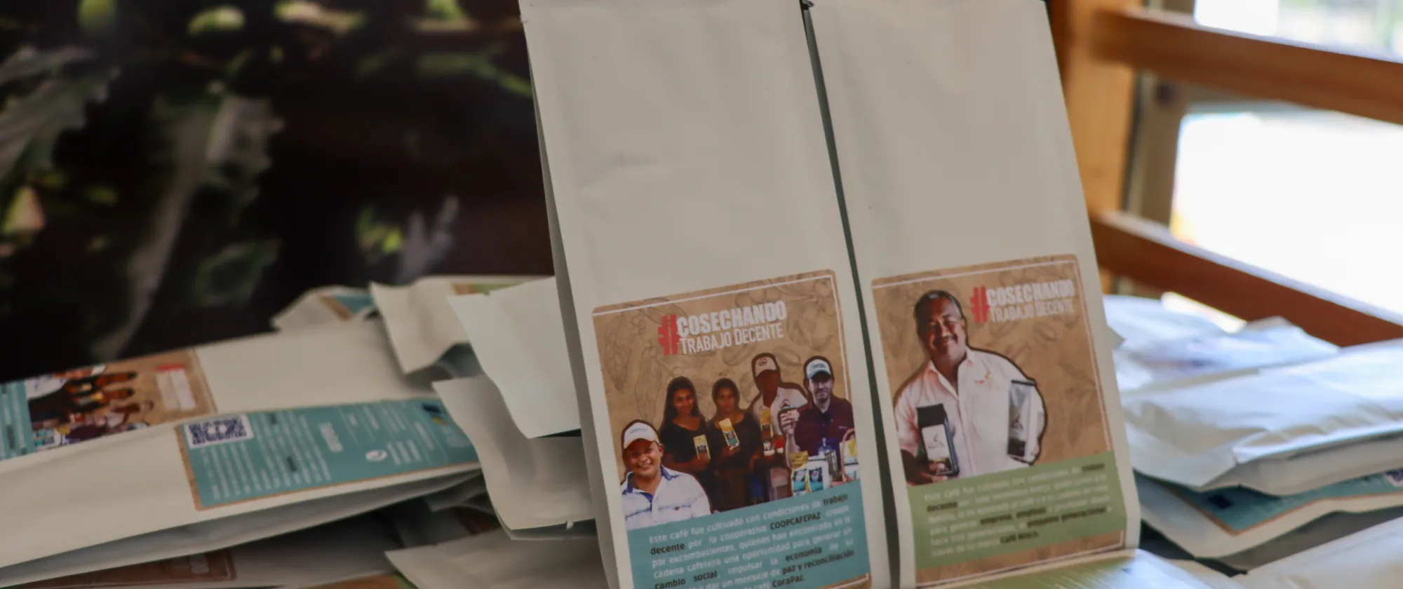 Bolsas de café blancas de aproximadamente 80 gramos con el etiquetado de #CosechandoTrabajoDecente, de las cuales la primera corresponde a Coopcafepaz, cooperativa de café conformada por excombatientes, y la segunda, perteneciente al productor José Ninco, quien impulsa el relevo generacional en su familia con su marca de café.