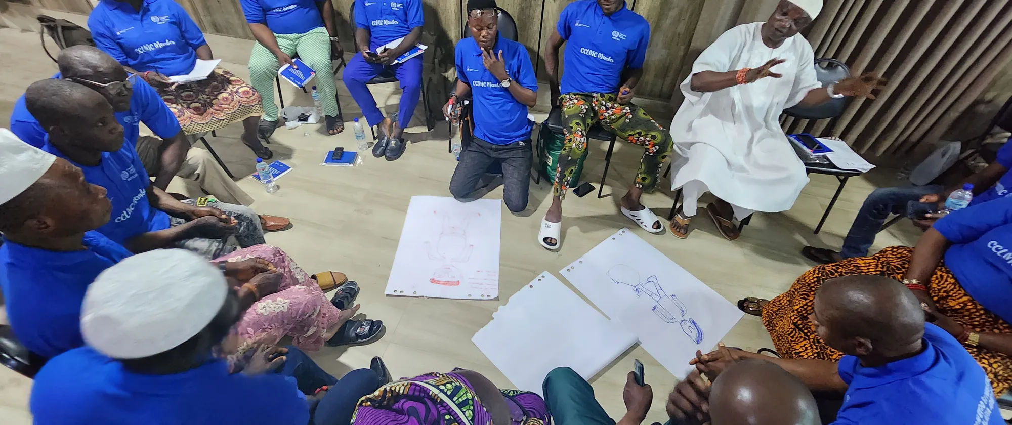Participants to a training seat in blue t-shirt in a round group and look at white pieces of paper, while one of them in white explains the concept of child labour