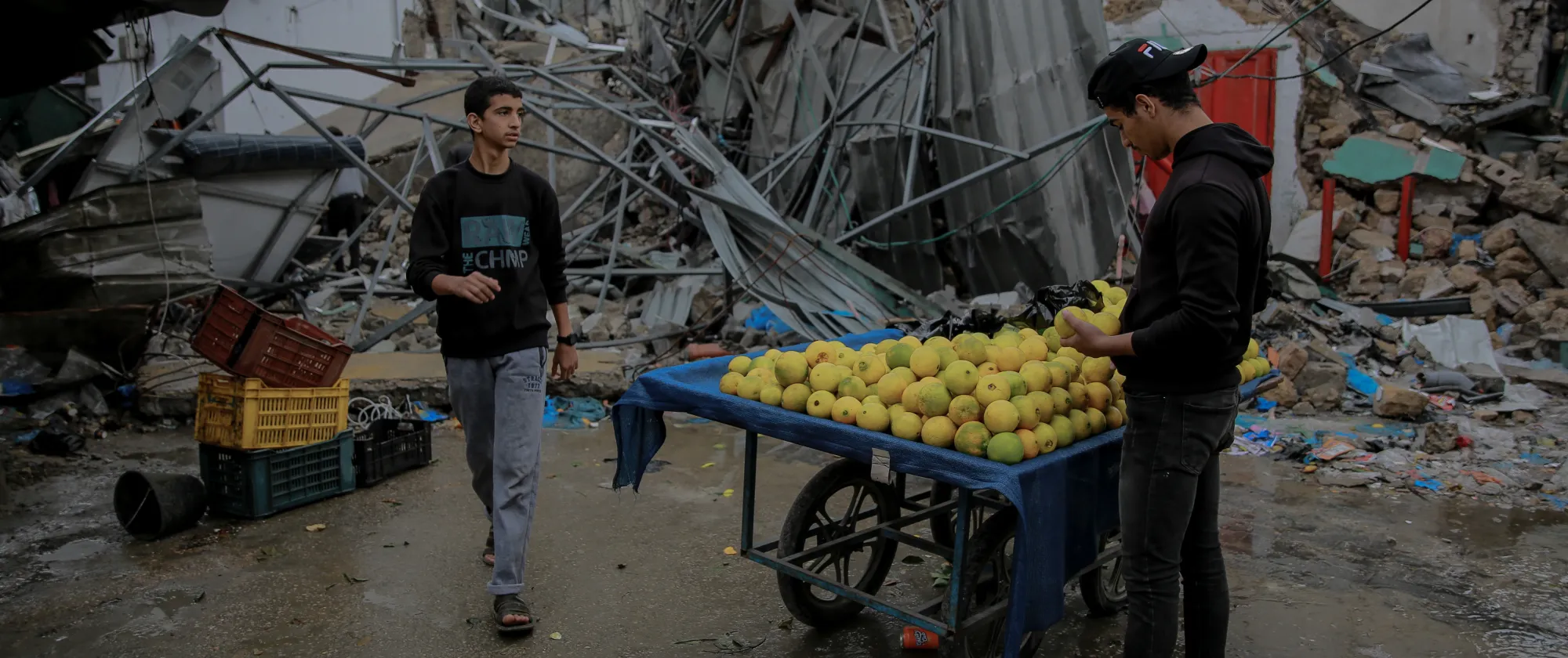 Young man sells oranges in front of a commercial shop destroyed by bombardment in the historic Azzawieh Market in Gaza City.