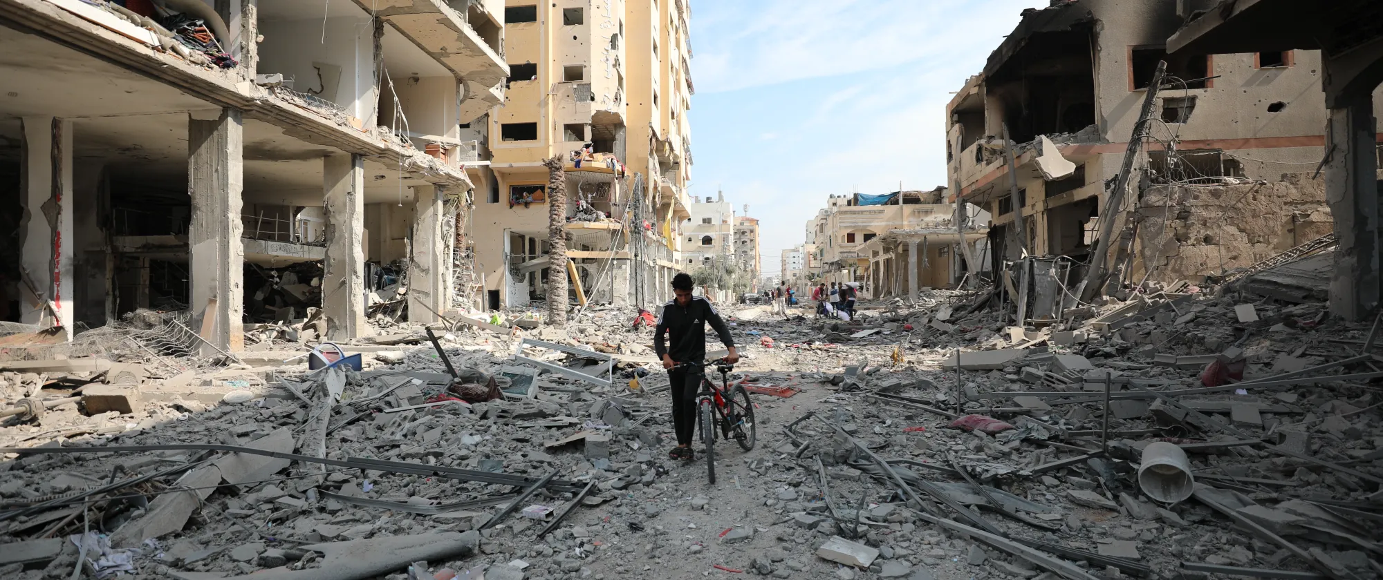 a young man dragging his bicycle among the extensive destruction caused by the airstrikes on Gaza.
