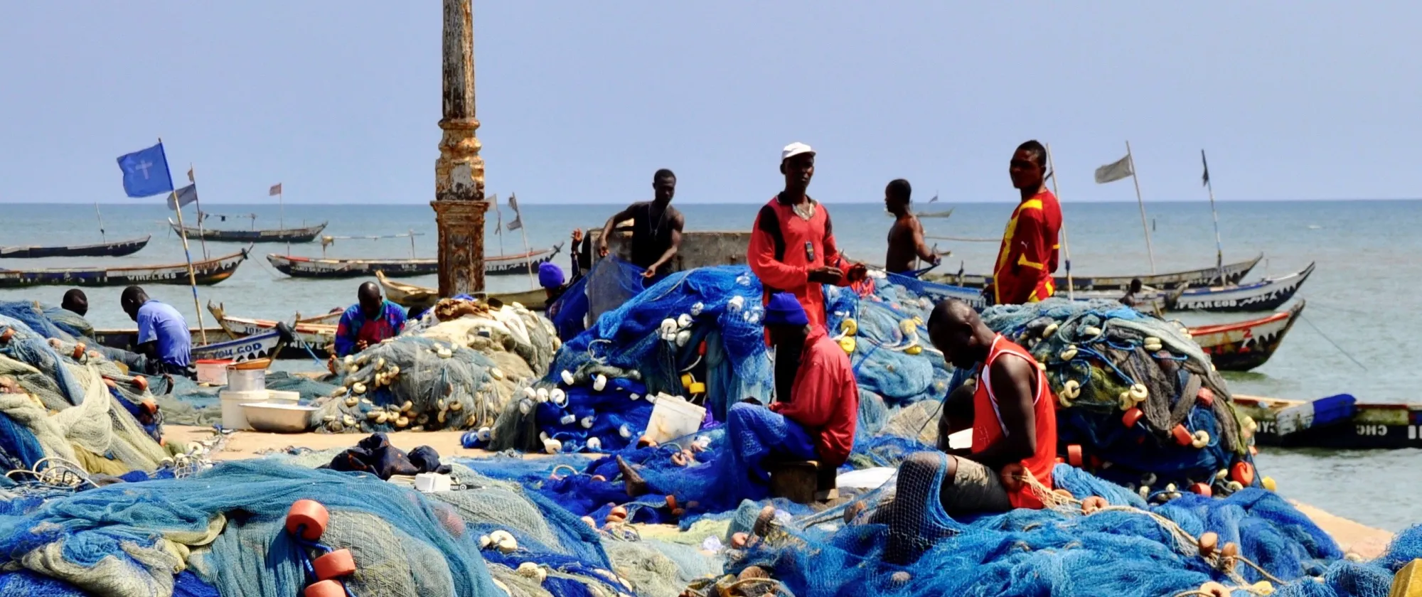 Some fisherman are working with fishing nets in a harbour in Côte d'Ivoire, they are wearing red shirts and the fishing nets are blue