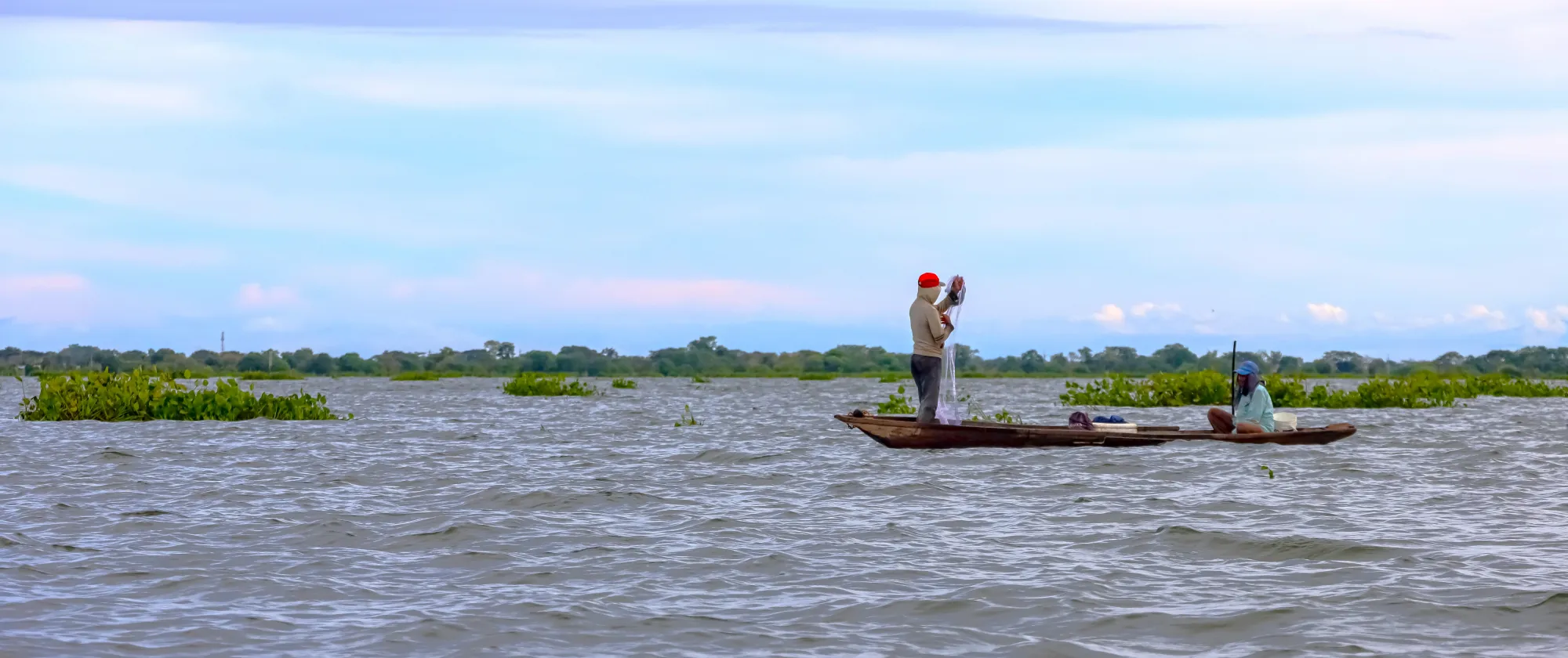 Dos pescadores sobre una panga en un río ejerciendo su labor.
