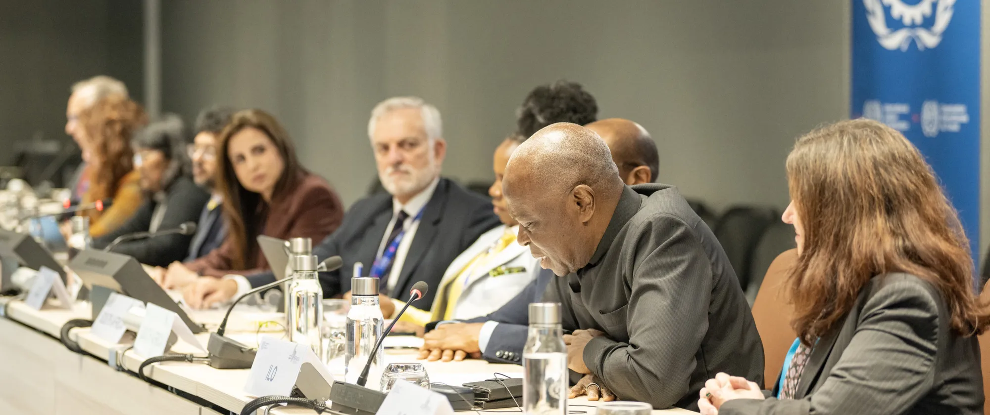 Row of men and women behind a long desk with the ILO logo behind them