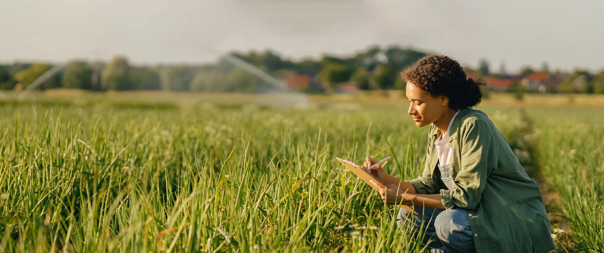 Female farmer writing on a clipboard while sitting in a field during harvest