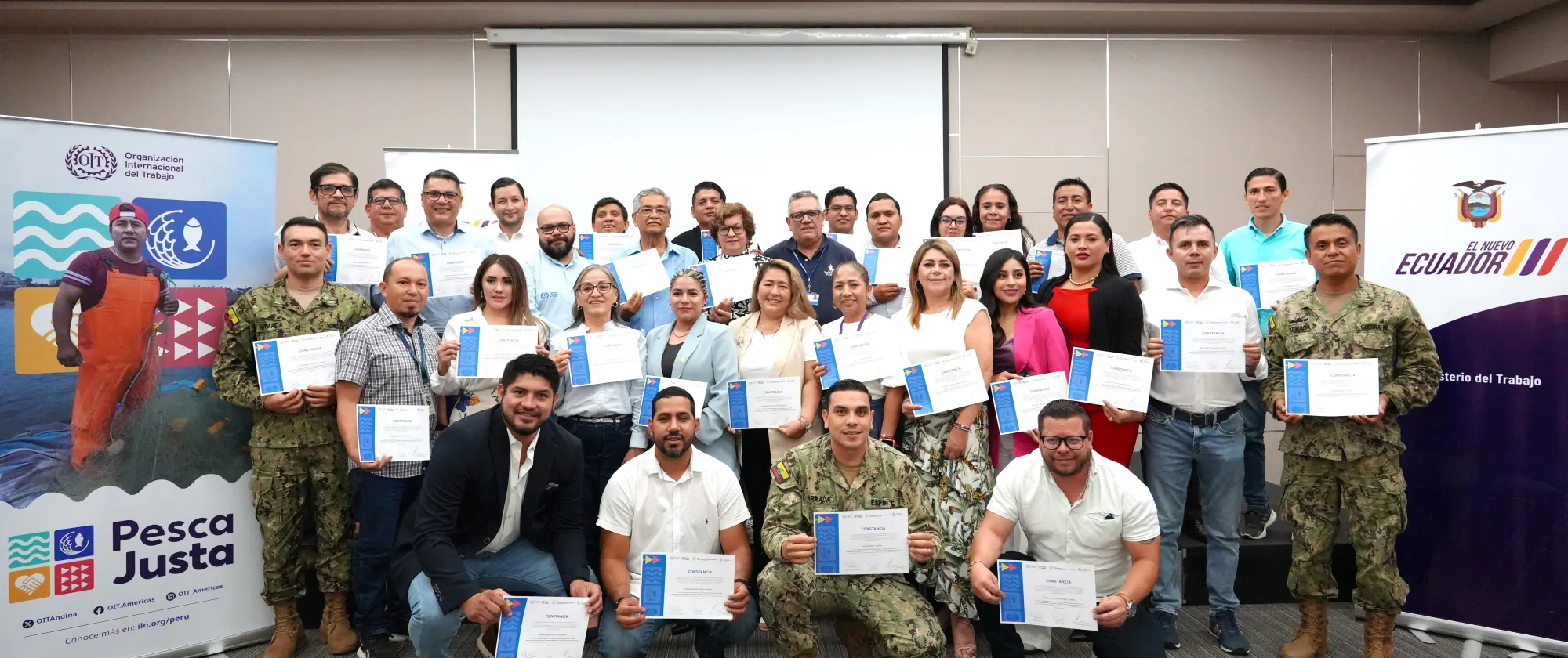 Grupo de personas sonrientes sosteniendo un diploma junto con los banners de OIT "Pesca Justa" y el Ministerio de Trabajo del Ecuador
