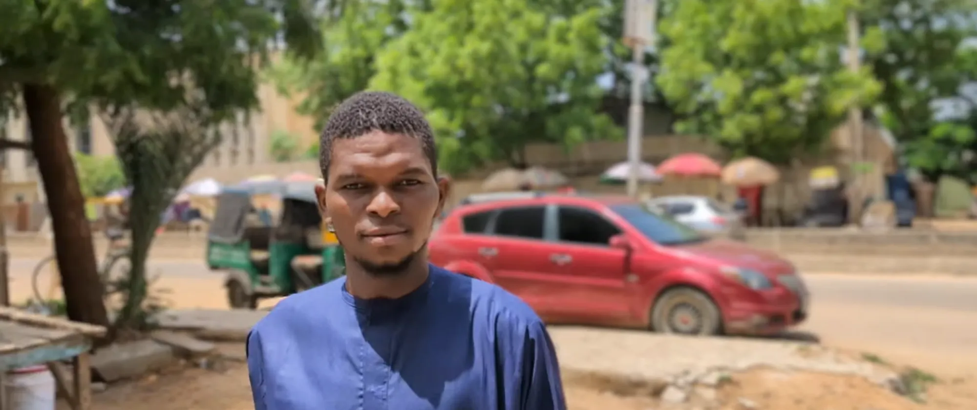 Usman Isah Abdullahi standing, with a vehicle and trees in the background