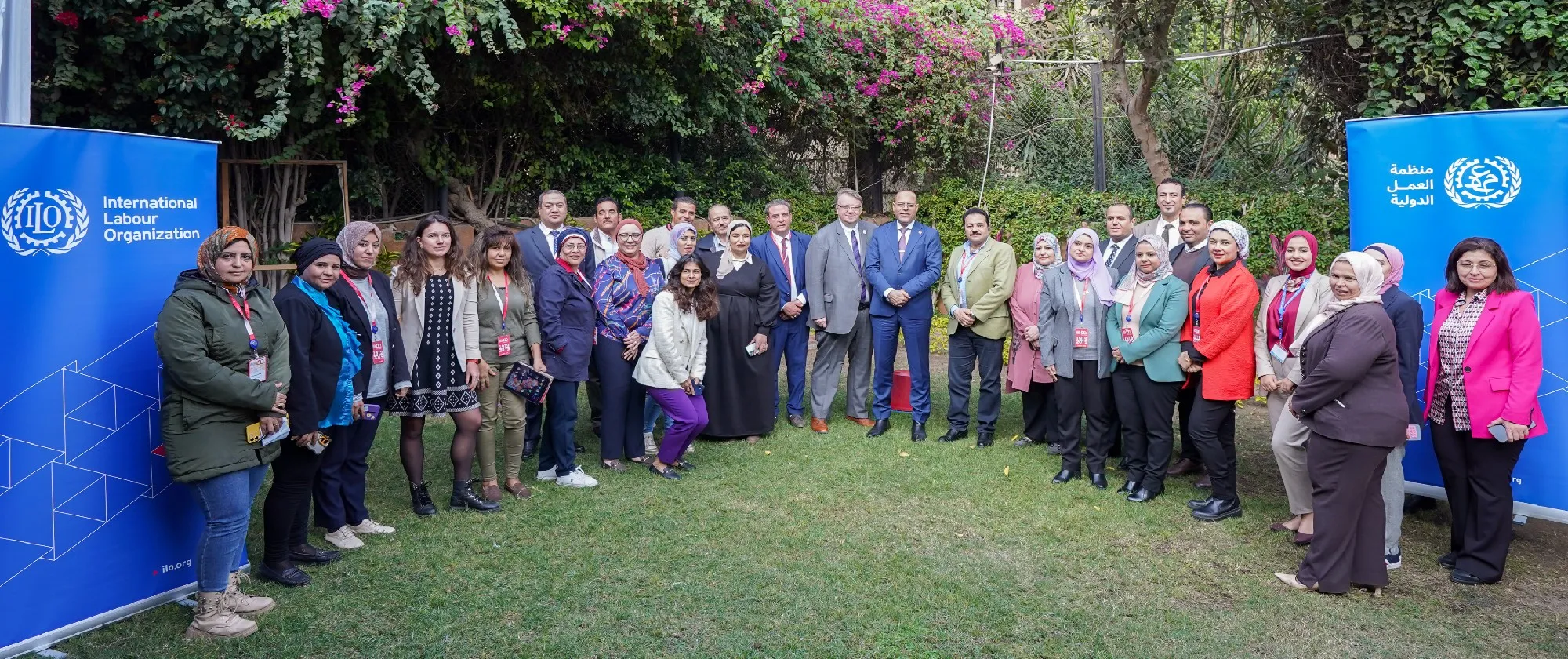 A diverse group of individuals stands together in front of a large blue banner, smiling and engaged in conversation.