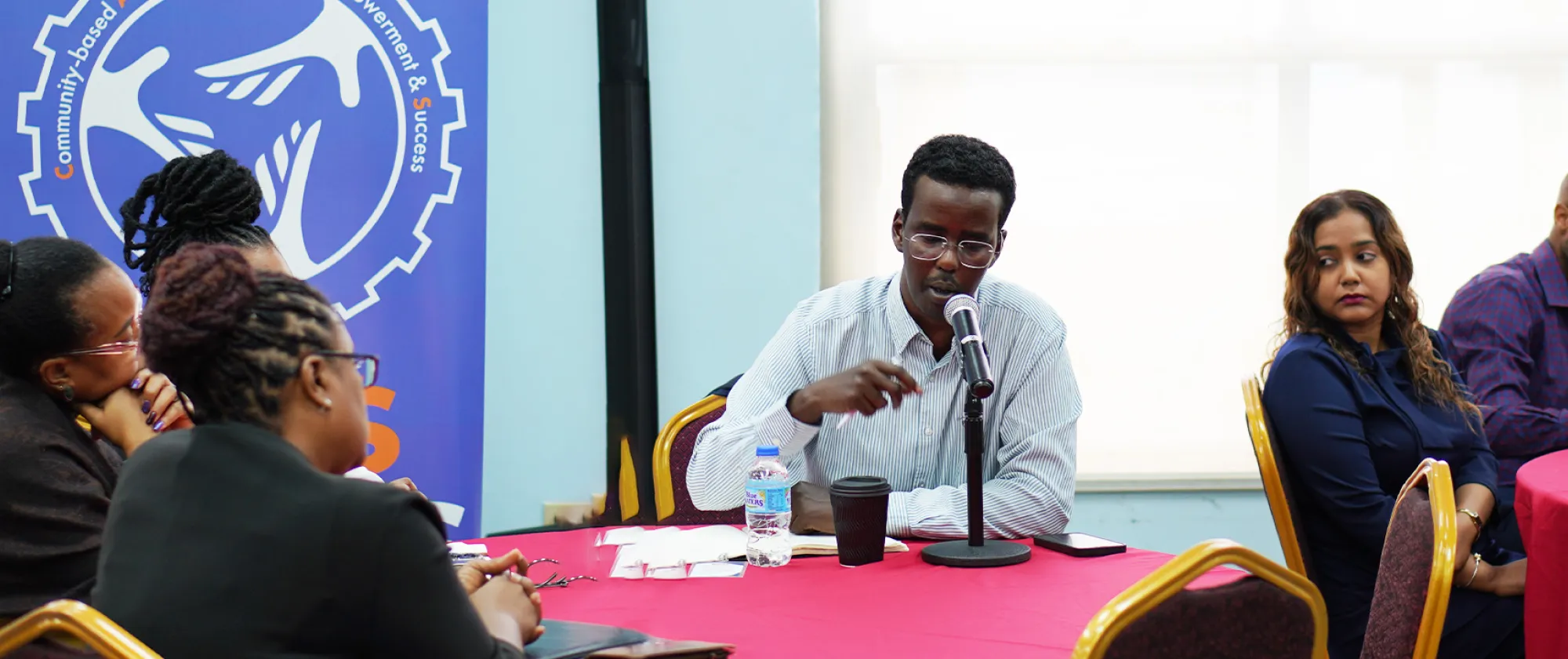 A man sitting on a table speaking on a microphone address participants at a meeting