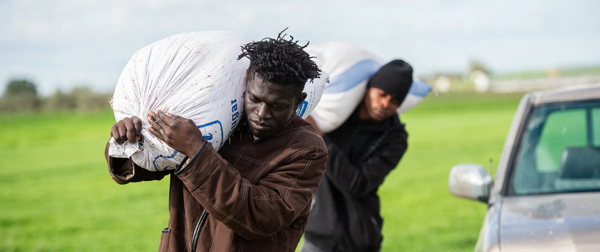 Two migrant workers carry heavy loads on their back