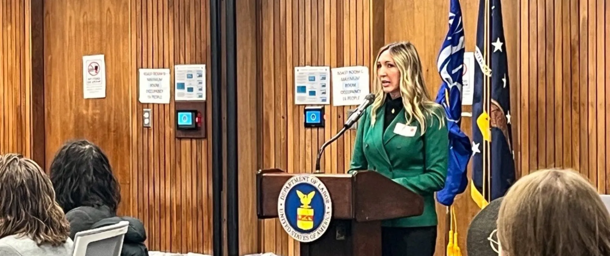 woman dressed in green speaking behind a podium to an audience