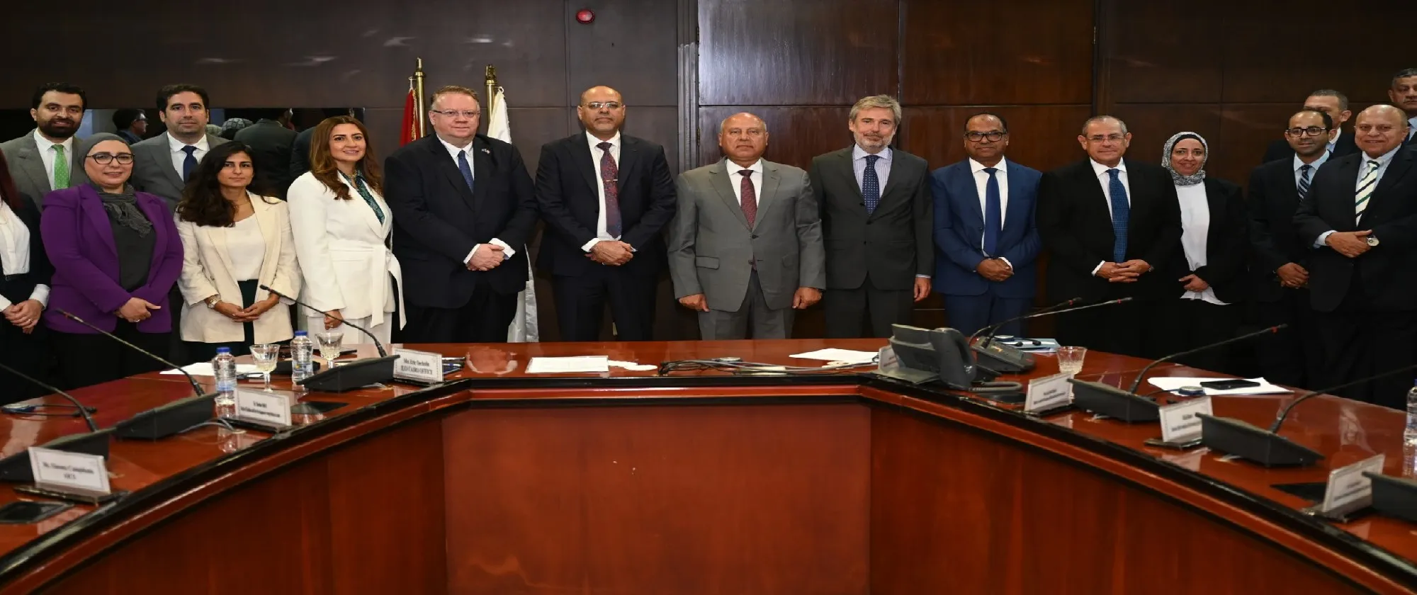 Group of diverse professionals in formal attire at a conference table during a business meeting, highlighting a collaborative corporate environment.