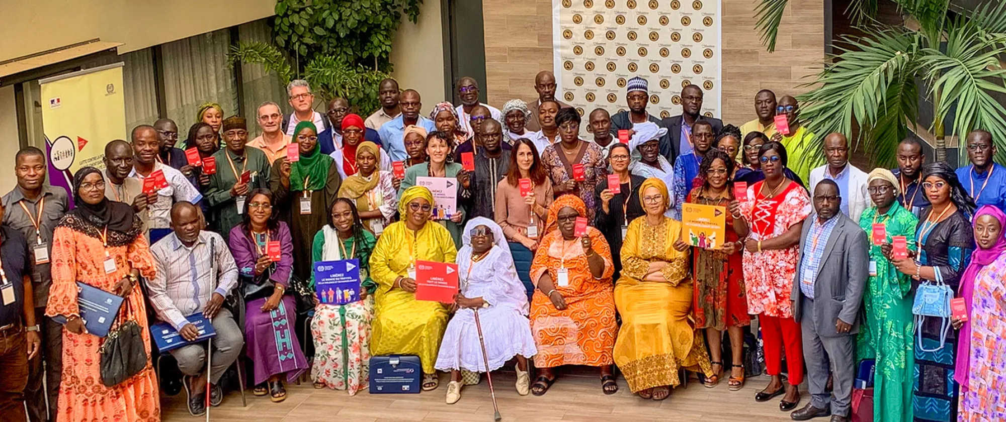 Photo de groupe lors d'une rencontre organisée à Dakar sur la prévention de la violence et du harcèlement dans le monde du travail. Les participants, représentant diverses parties prenantes, tiennent des brochures et des cartes rouges symbolisant leur engagement à promouvoir des lieux de travail sûrs, inclusifs et respectueux.
