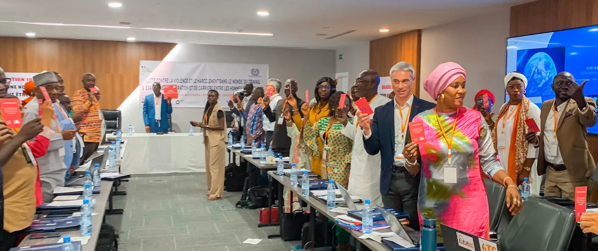Photo de groupe lors d'une rencontre organisée à Dakar sur la prévention de la violence et du harcèlement dans le monde du travail. Les participants, représentant diverses parties prenantes, tiennent des brochures et des cartes rouges symbolisant leur engagement à promouvoir des lieux de travail sûrs, inclusifs et respectueux.