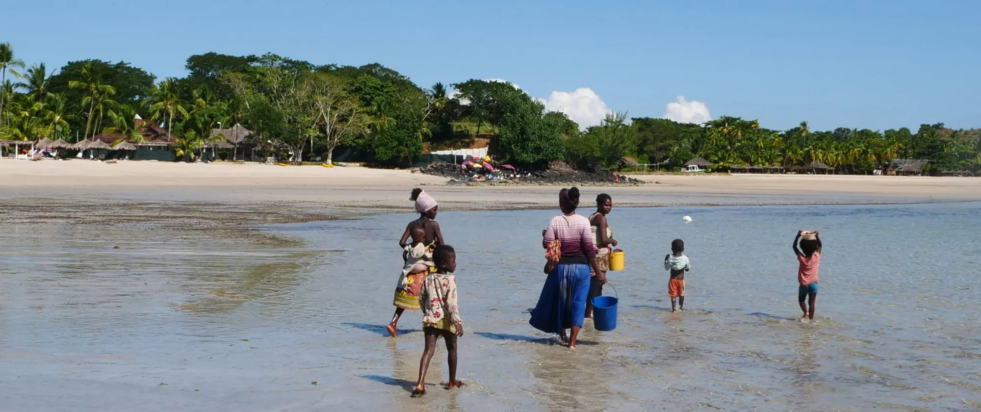 Des enfants et leur mère avancent dans l'eau transparente.