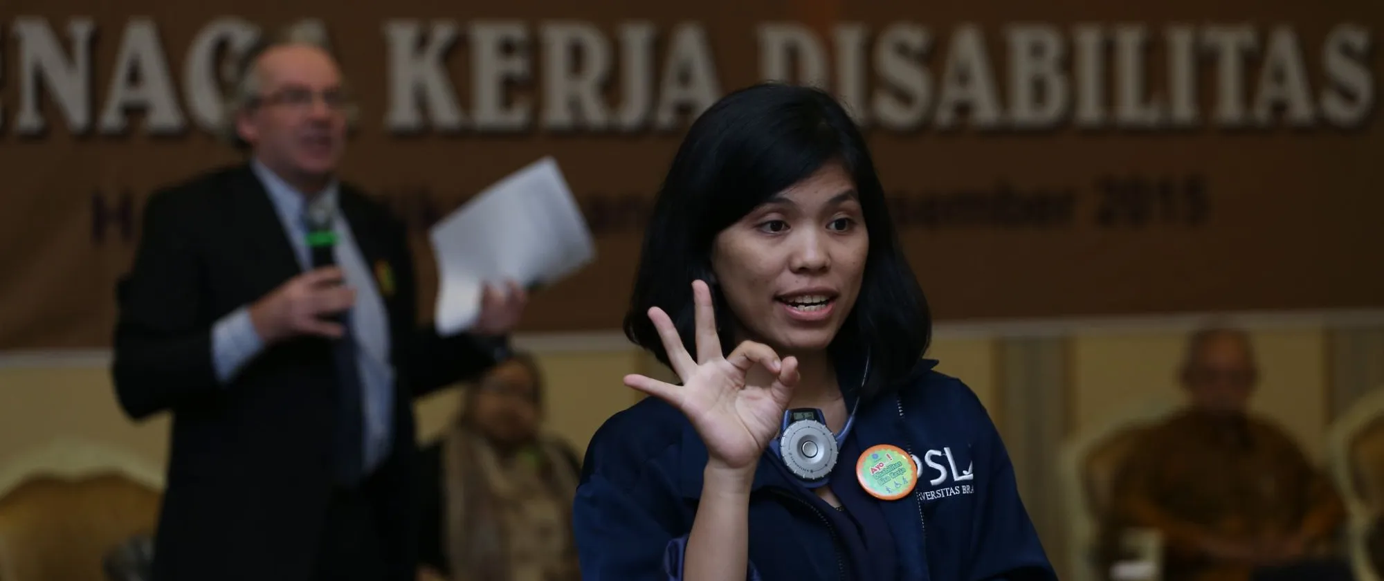 an Indonesian young woman using sign-language to a forum's audience
