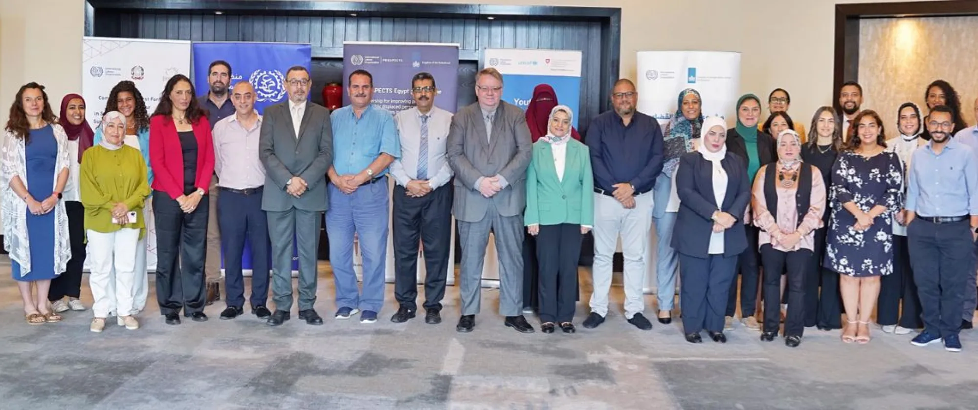 A diverse group of individuals smiling and posing together in front of a colorful banner at an event.