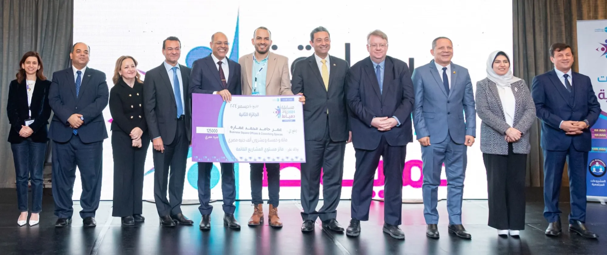 Several people stand on stage, holding a large check, symbolizing their collective success and accomplishment.
