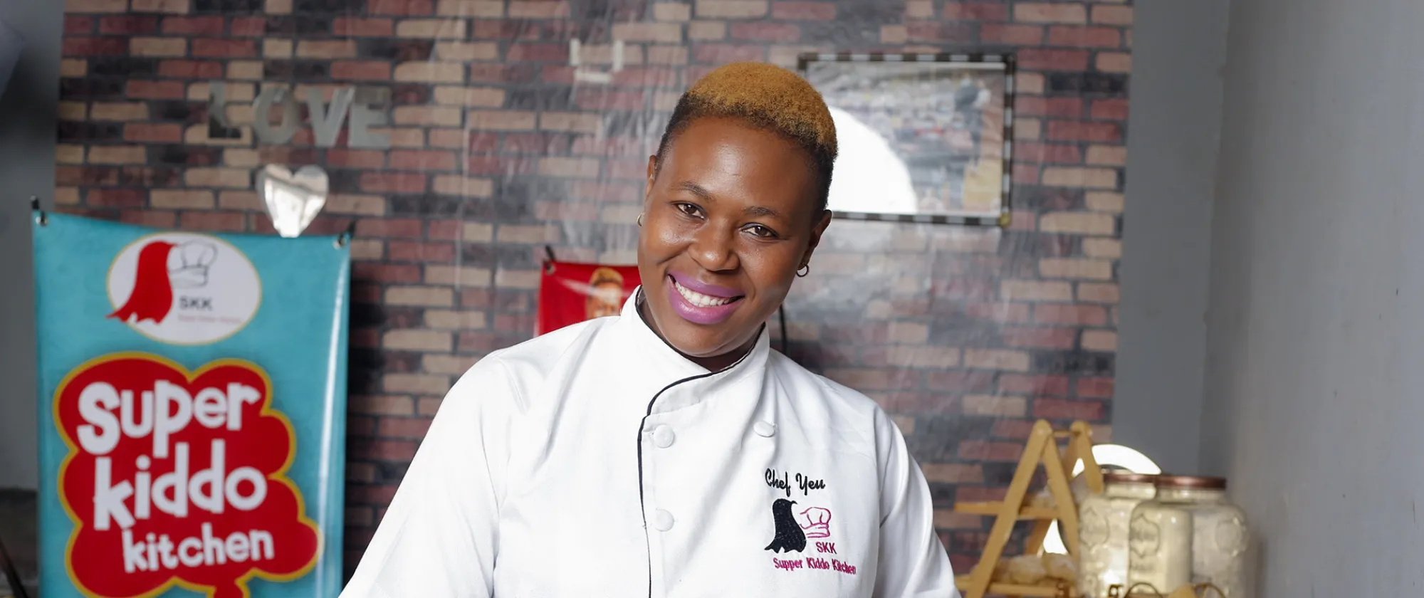 Yeukai Maposa, the founder of Super Kiddo Kitchen in Zimbabwe, stands in her kitchen looking straight at the camera.