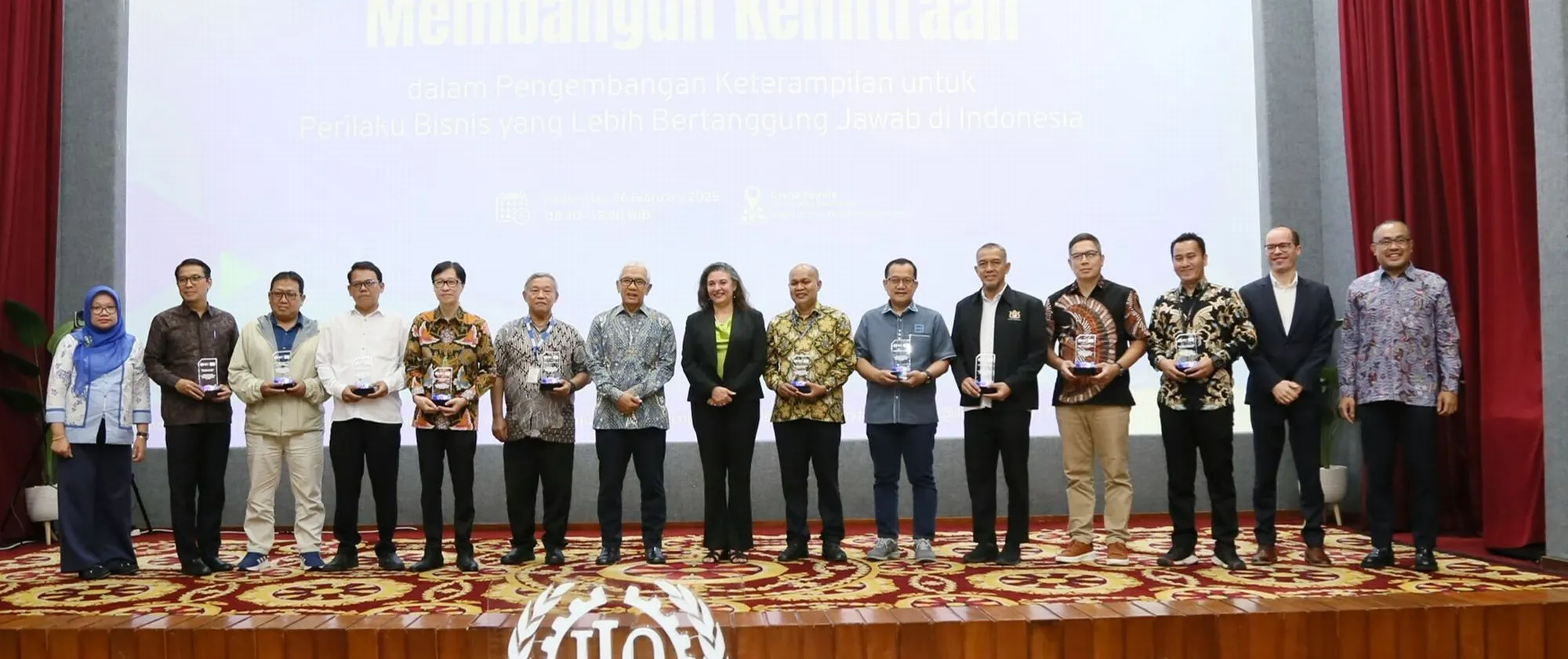 A group photo of 15 people standing on the stage with the ILO logo in font of them.
