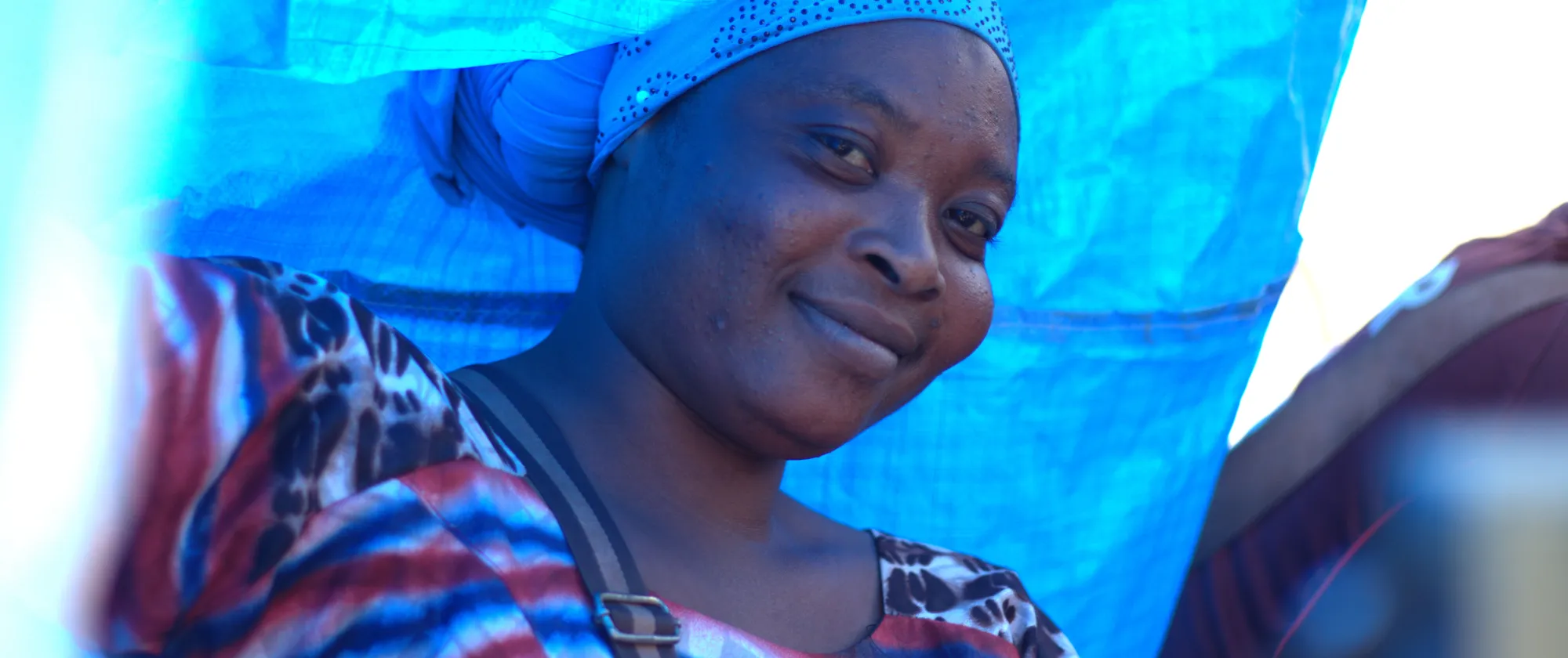 A Malian lady looks with a smile under a blue tent 