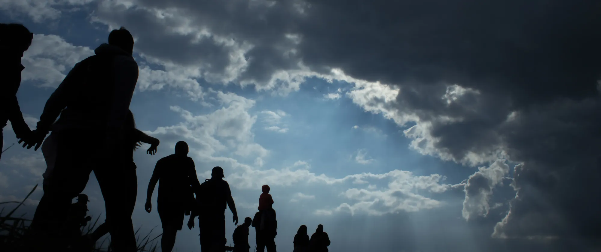 Sun rays illuminate people. Immigration of people. Blue sky with dark clouds.