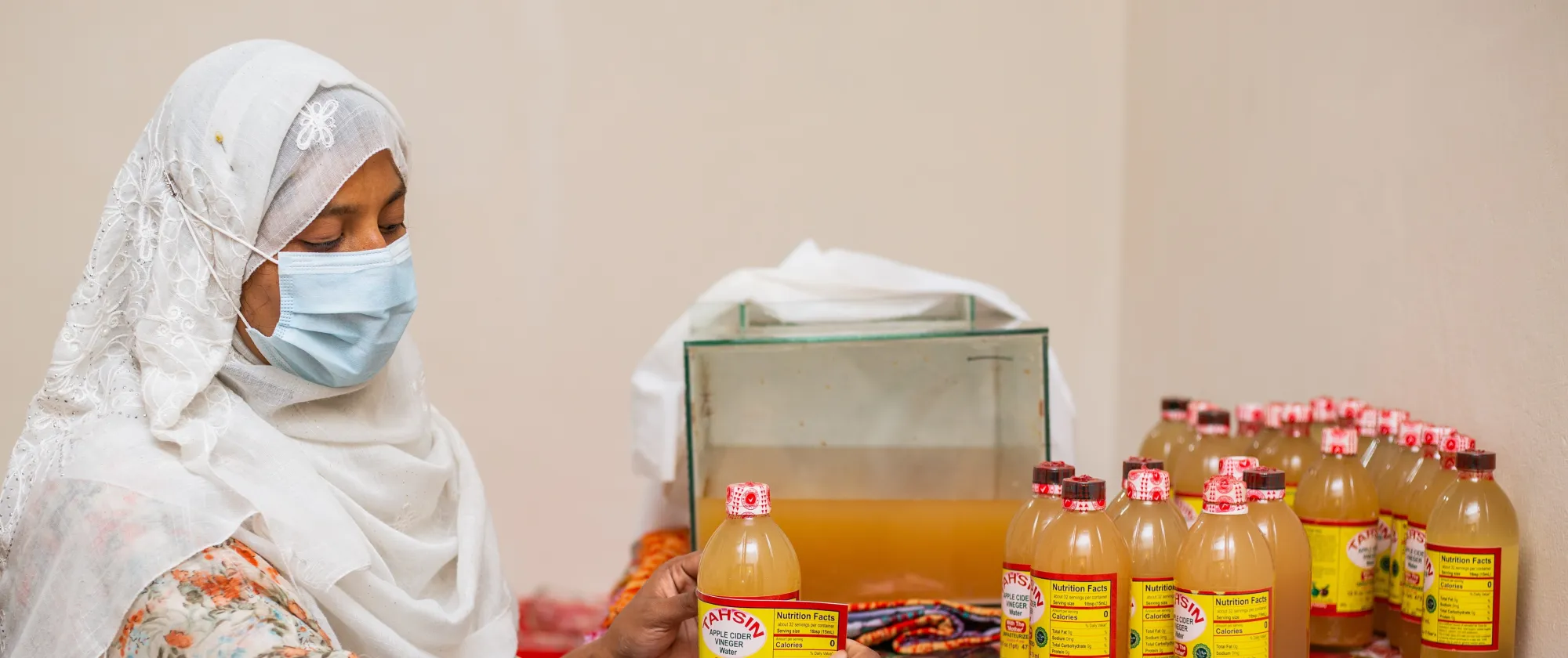 A lady wearing a mask is labelling a bottle.