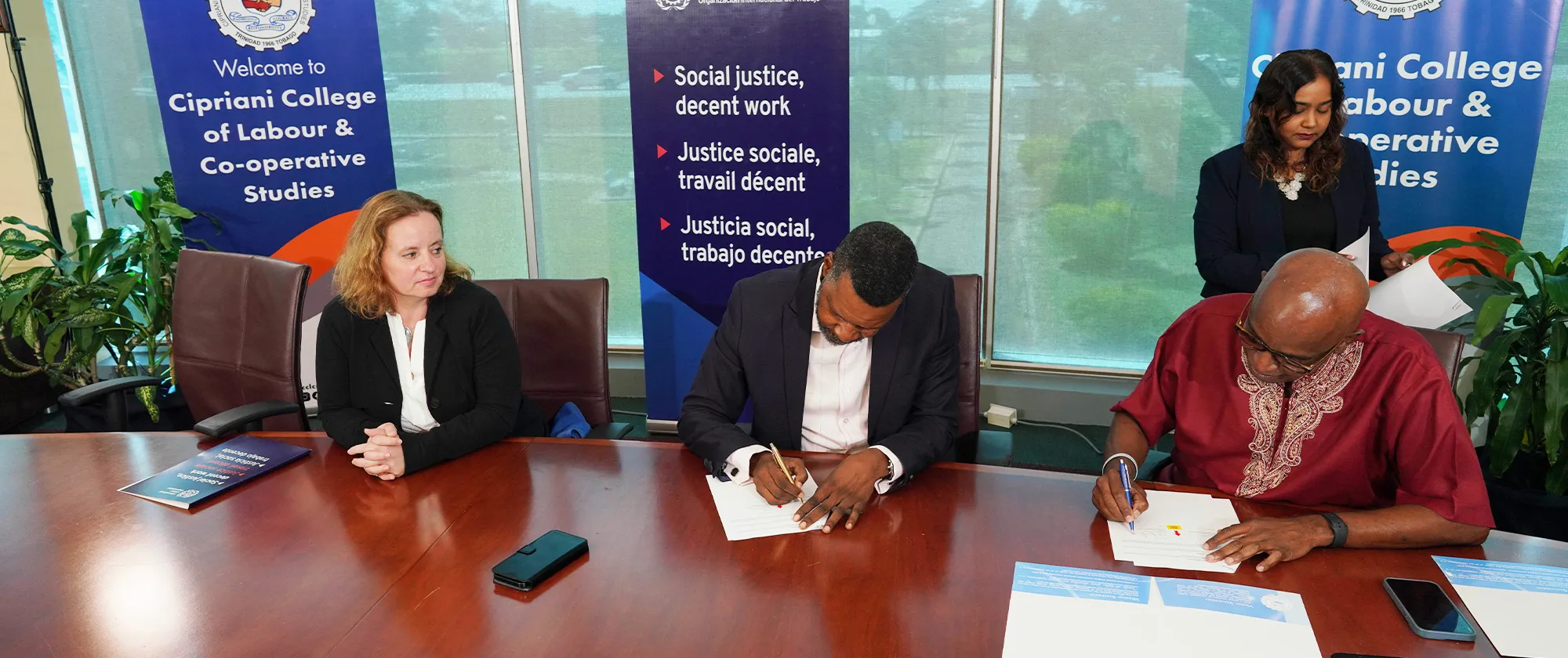 Three persons sitting at a table with two men signing documents