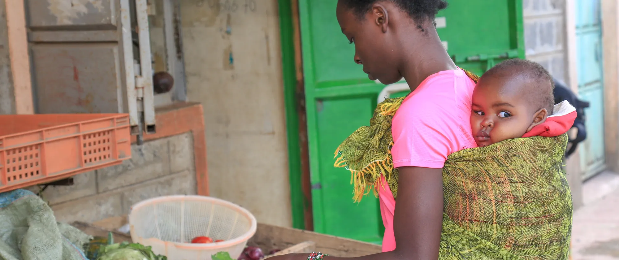 A woman carrying her baby as she works in her vegetable stall