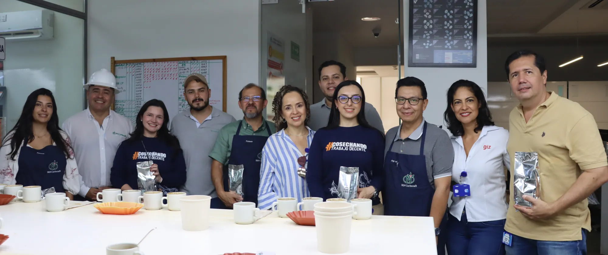 Grupo de once personas (seis hombres y cinco mujeres) posan para una foto en un laboratorio de café. 