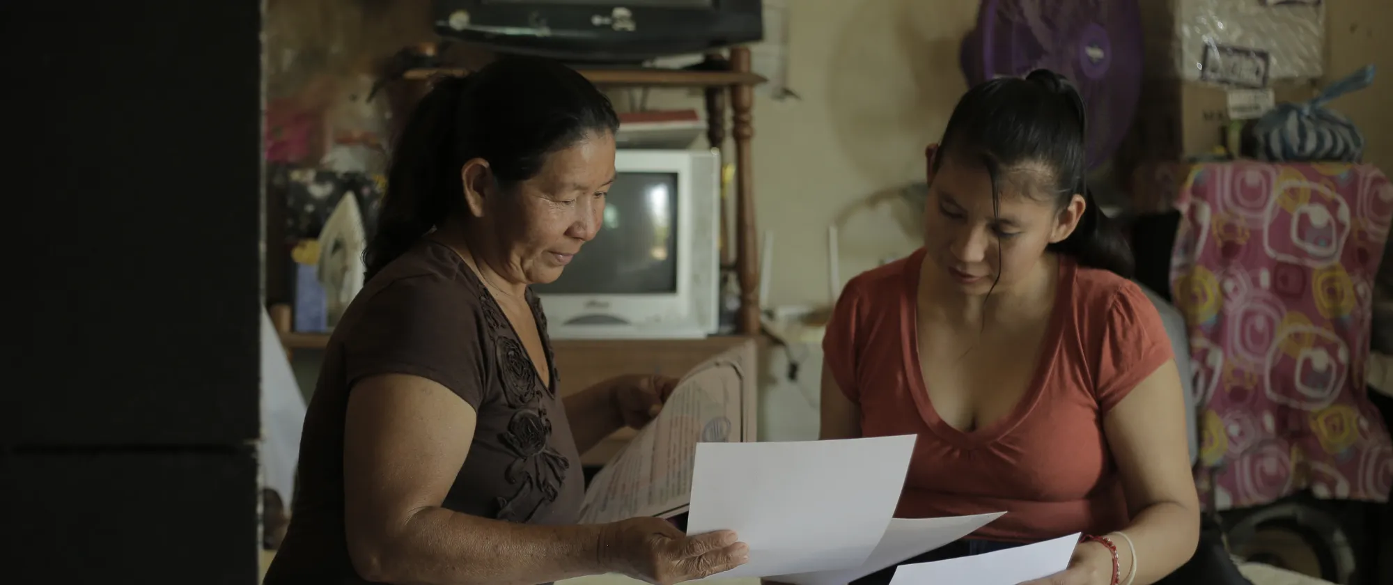 Dos mujeres sentadas en una habitación observando algunos documentos impresos.