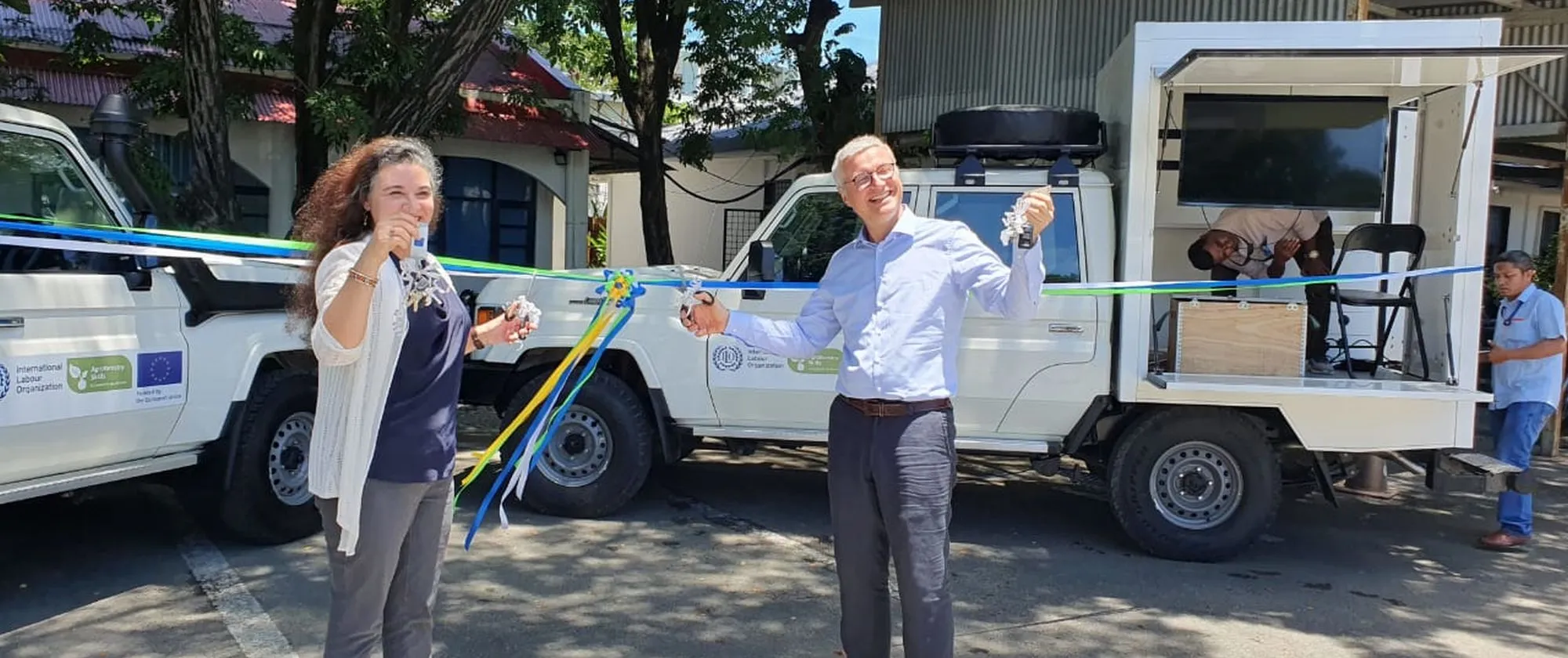 Two persons smiling with two mobile training unit behind them.