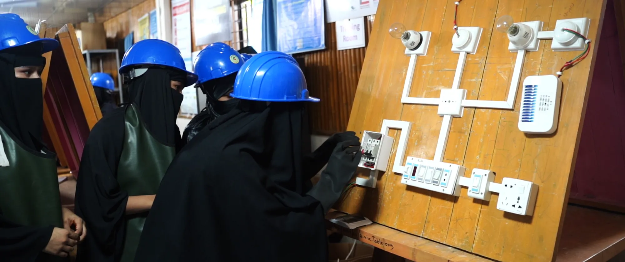A group of women in safety helmet gathered at an electrical circuit board