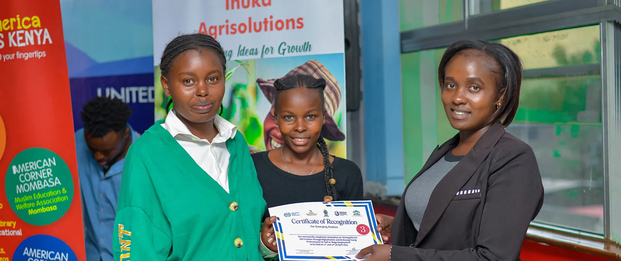 Three young women stand proudly holding a certificate of recognition at an ILO digital hackathon in Kenya aimed at addressing youth unemployment.