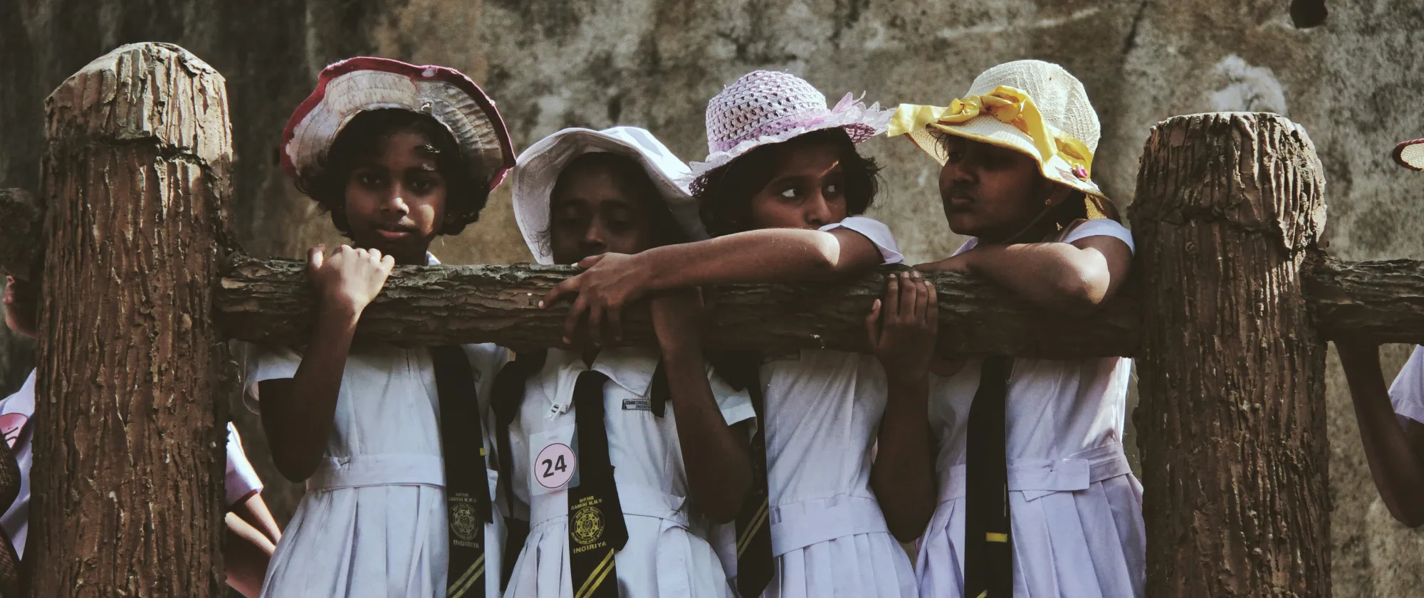 four young children in school uniform stand in a row behind a wooden railing