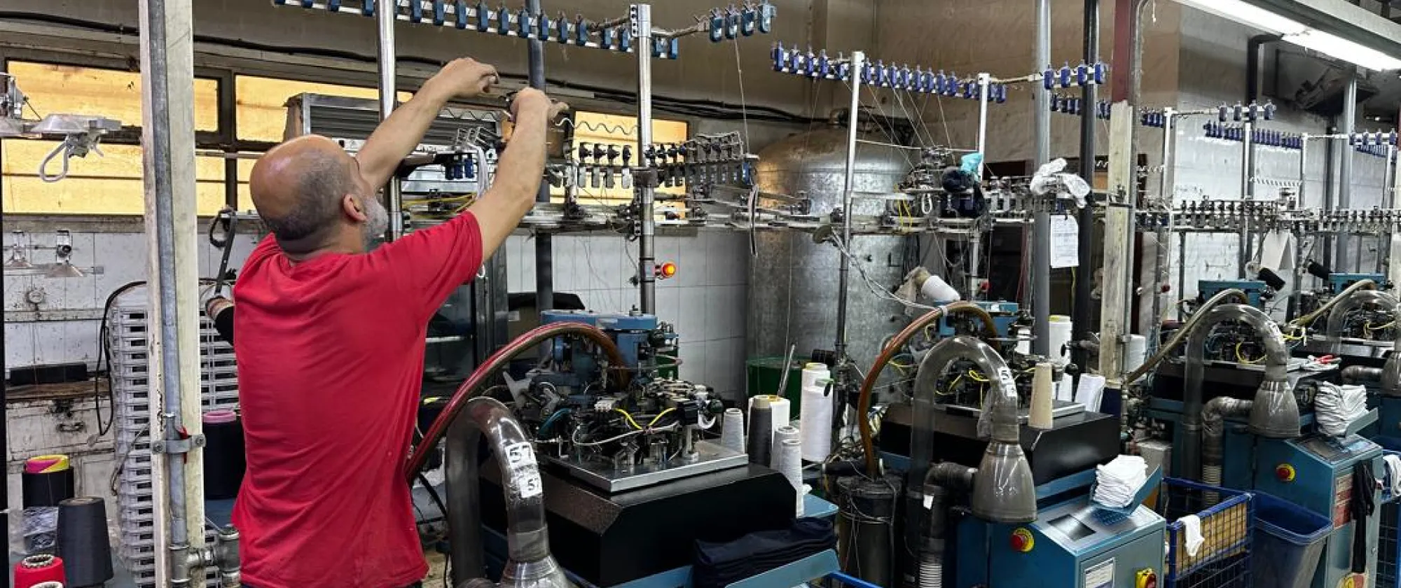 A man reaches over top of a machine at a textile factory in Syria