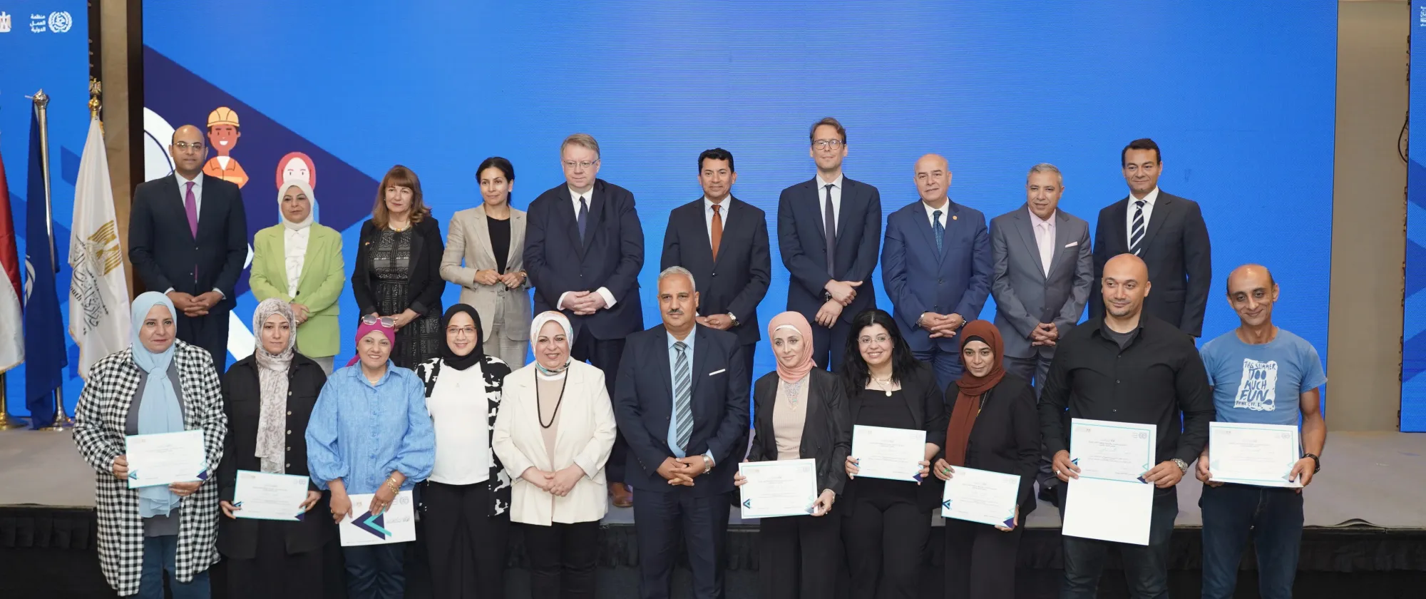 A formal group photo showing facilitators of the Job Search Club training programme holding certificates of recognition. They are joined by officials from the ILO, the Ministry of Youth and Sports, and development partners, standing in front of a blue backdrop at the award ceremony.
