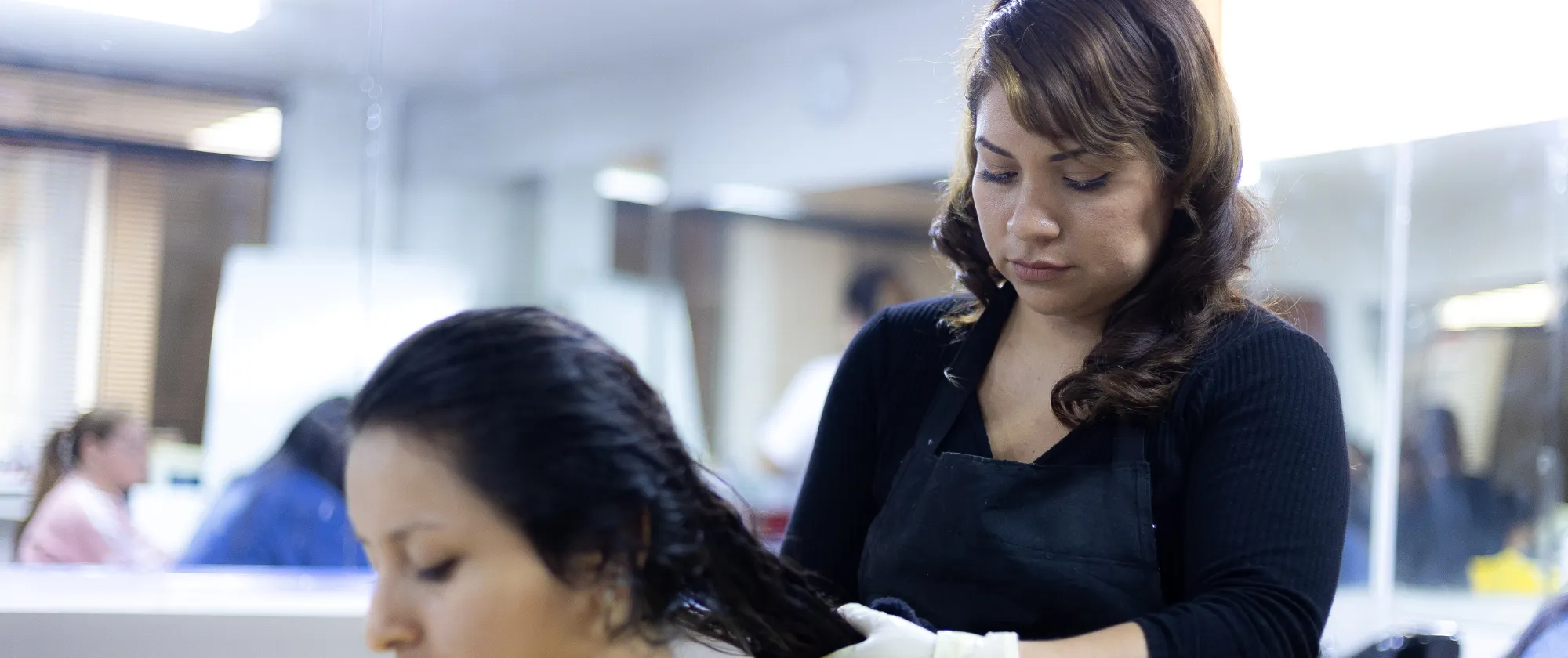 Mujer adulta estilista que corta el pelo a otra mujer adulta sentada, dentro de un salón de belleza.