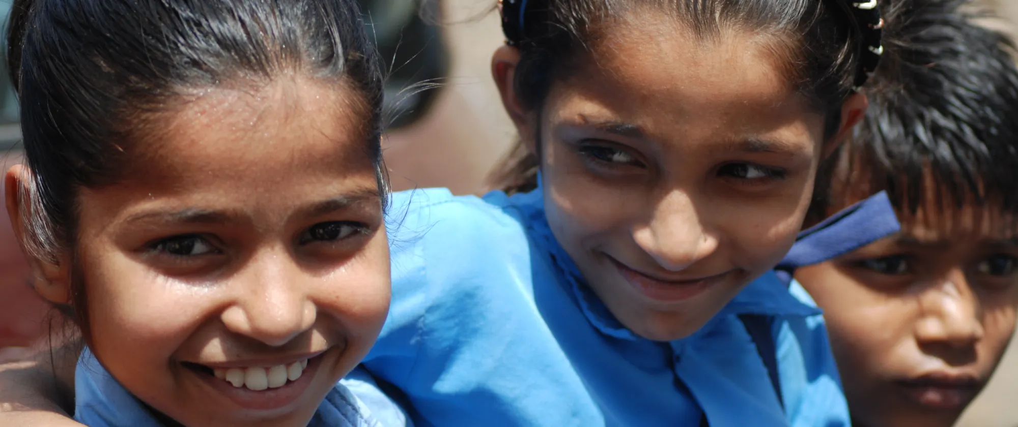 Two young girls and a young boy, smiling, wearing blue shirt uniform