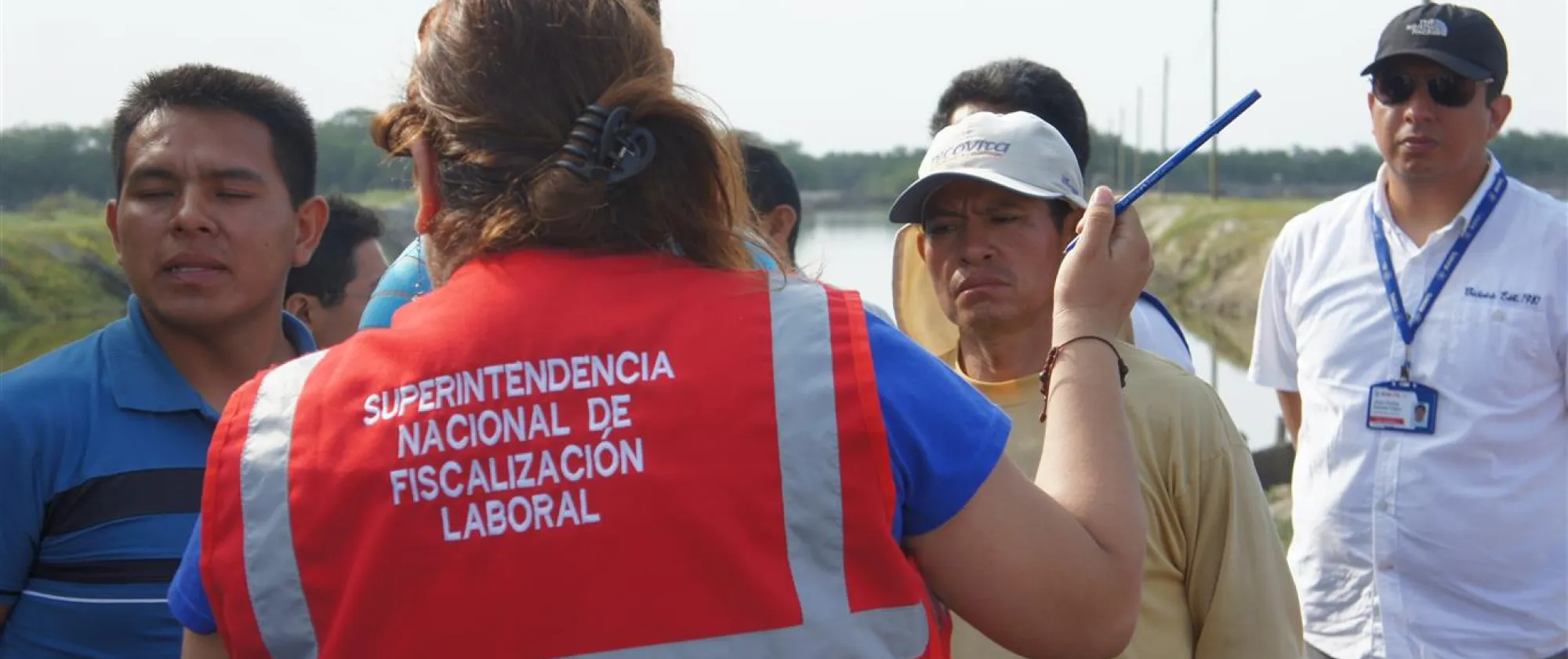 A woman labour inspector from Peru is seen from the back talking to a group of workers