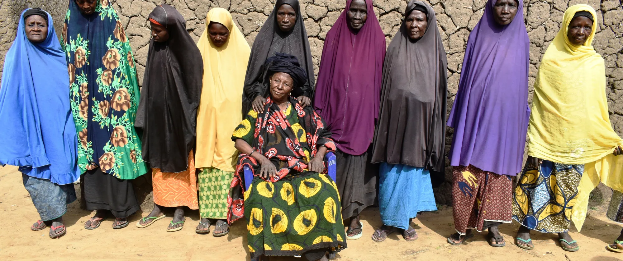 A group of women from Niger are standing in line behind their village leader seating in a chair