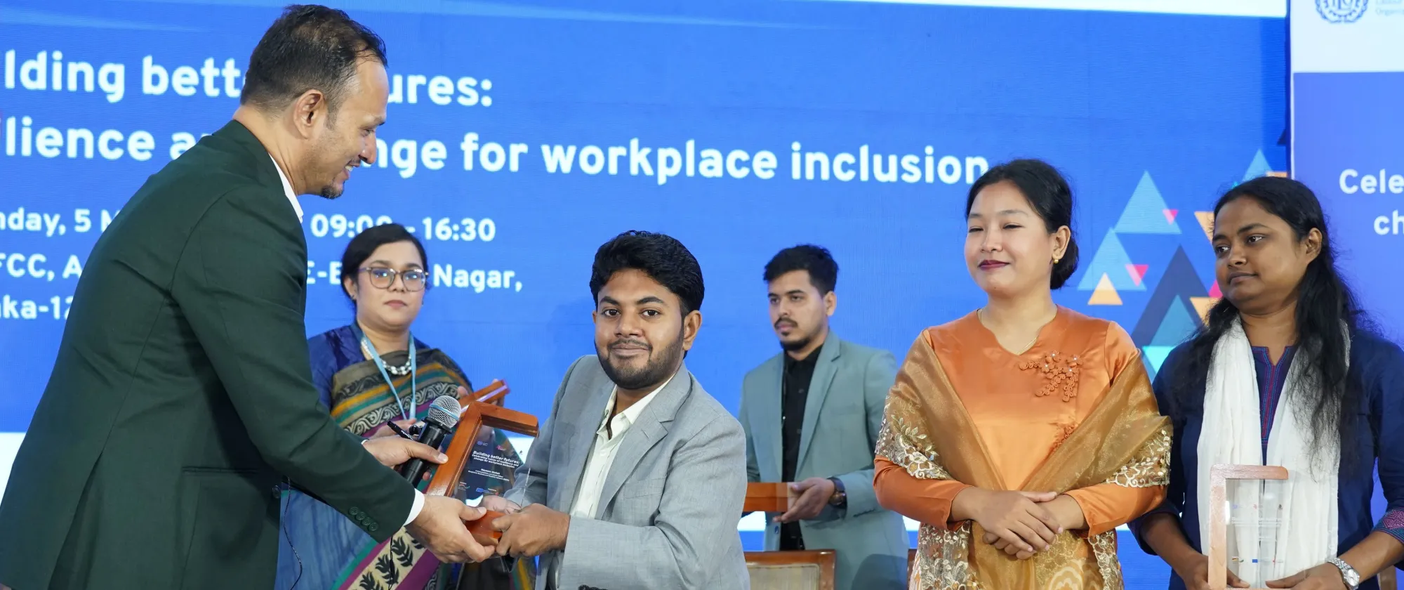 A male university student is presented with an honorary plaque as others look on