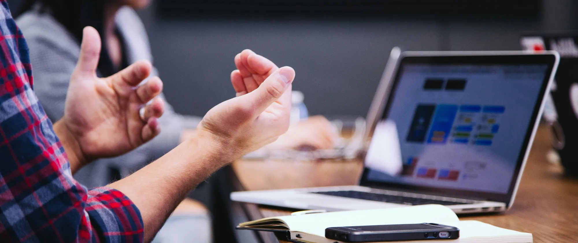 Focus on a persons hands, note book, phone and laptop