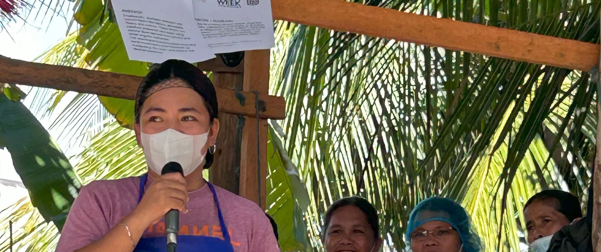 Jonalyn is wearing a blue apron and speaking over a microphone.